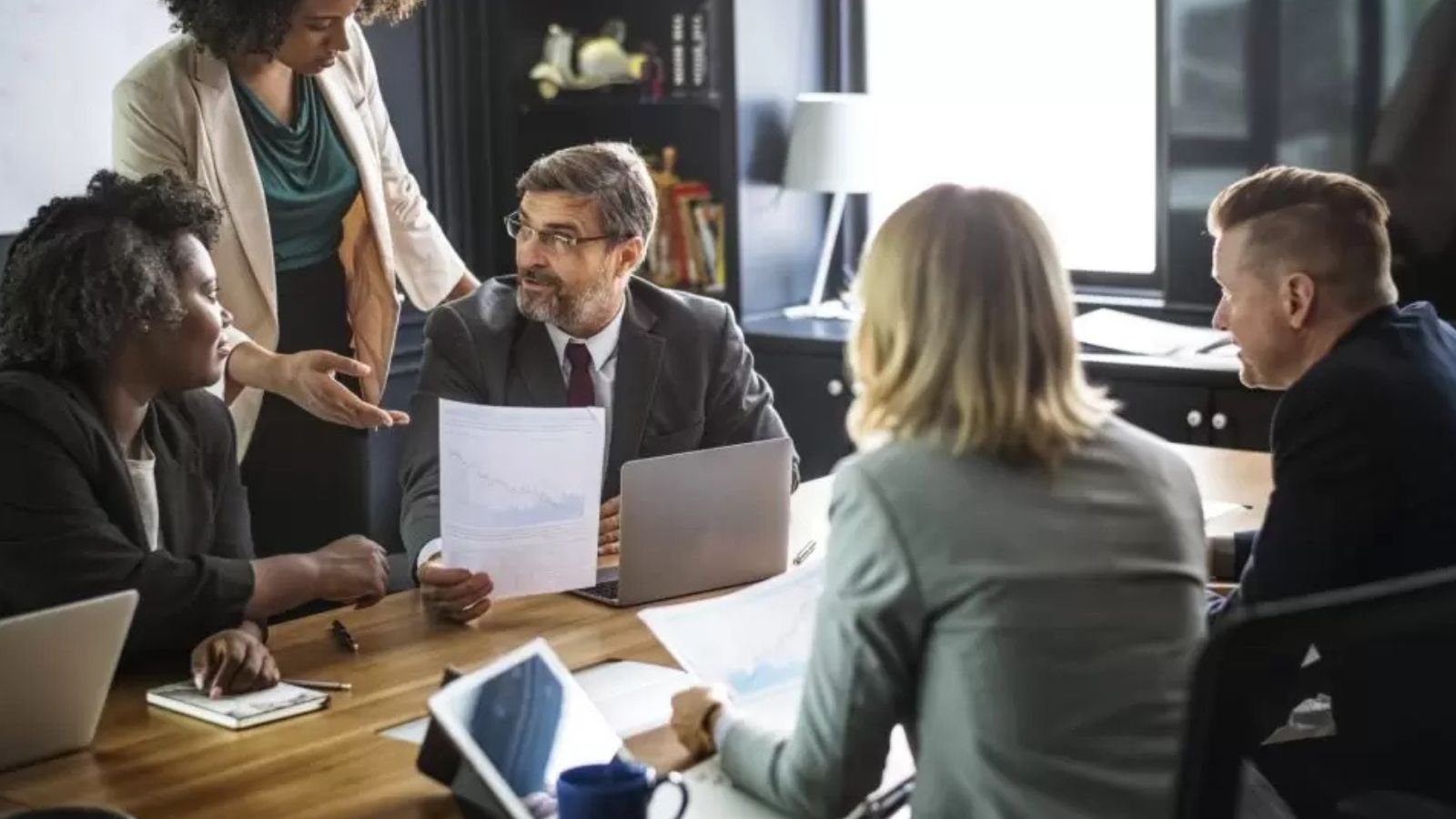 Um grupo de pessoas entre homens brancos e mulheres brancas e negras conversando no trabalho