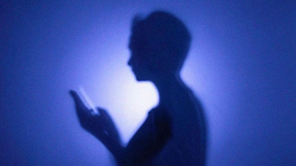 Silhueta de uma pessoa segurando um celular nas mãos