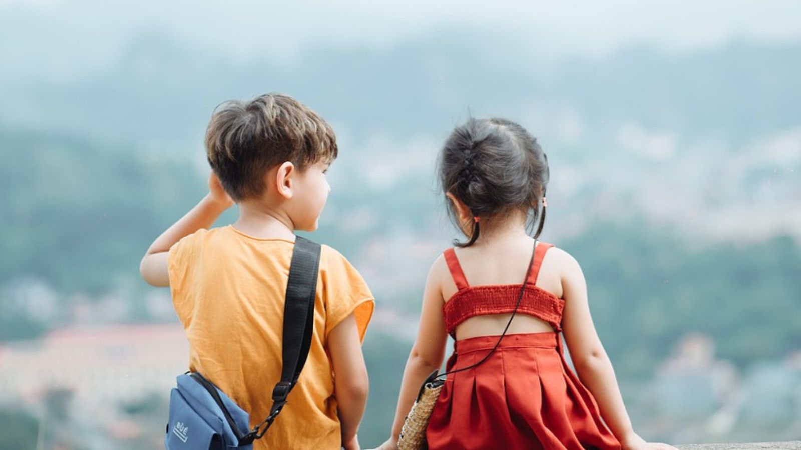 Um menino e uma menina de costa para paisagem