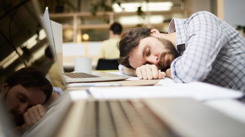 Homem com cabeça baixa em cima de notebook no serviço