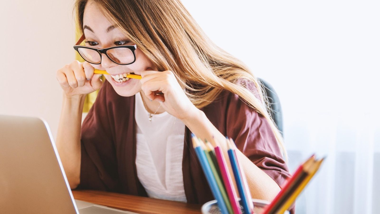 Mulher mordendo lápis em frente a notebook