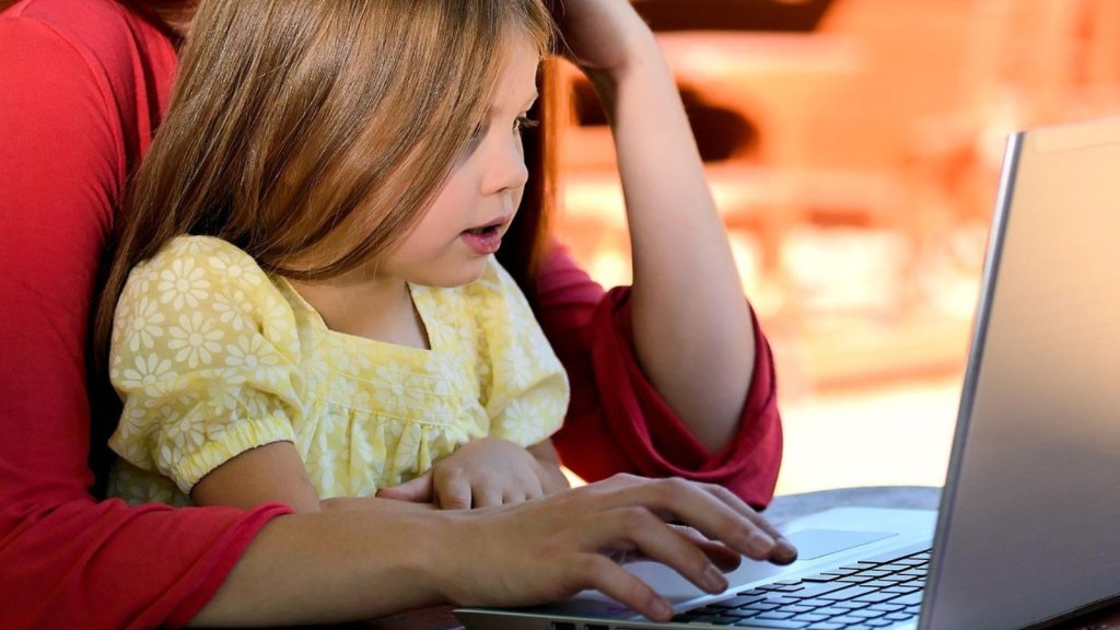 Mulher com filha no colo em frente a notebook
