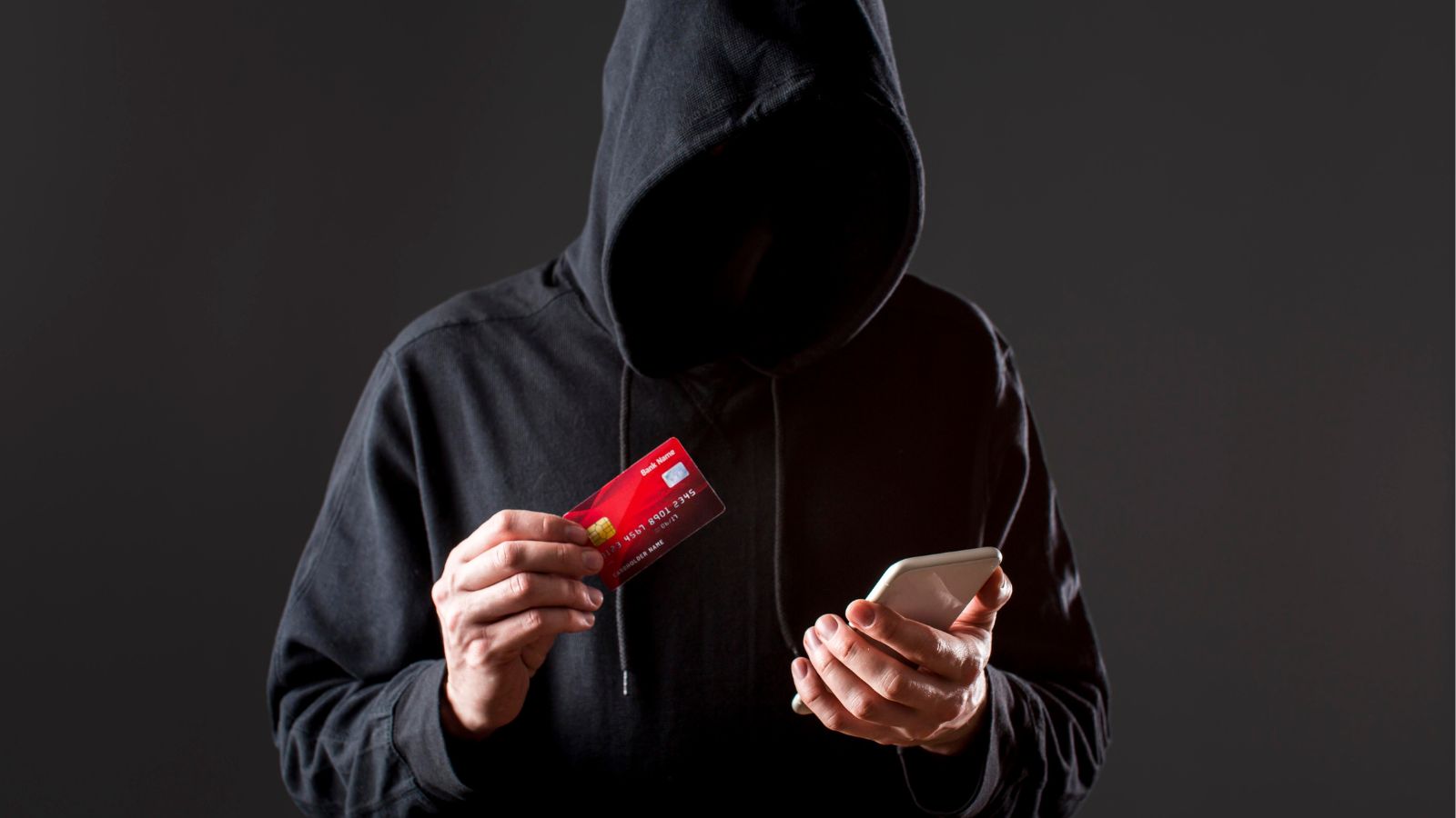 Homem de capuz segurando celular e cartão em fundo preto