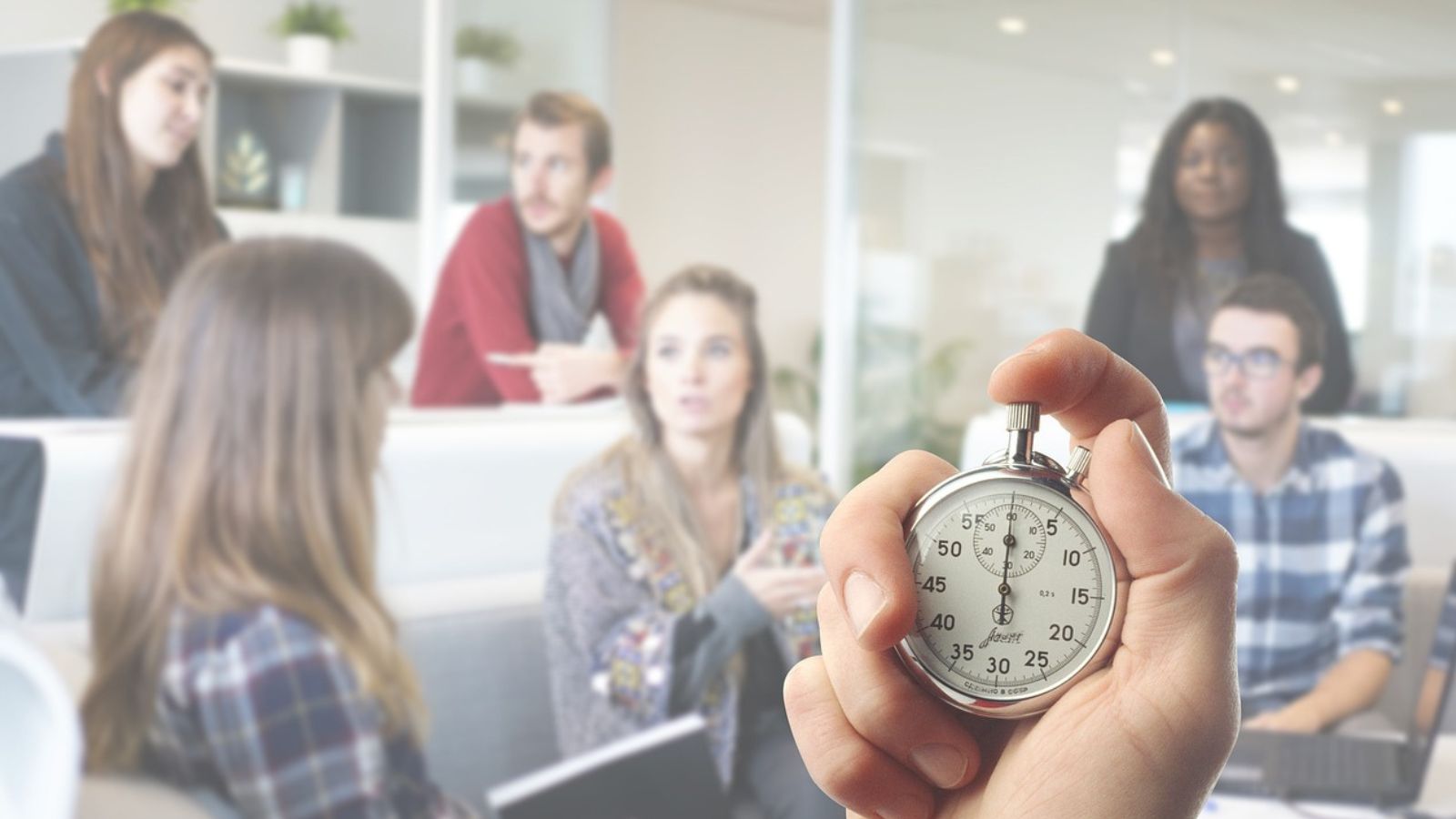 Pessoa segurando relógio e equipe de trabalho ao fundo