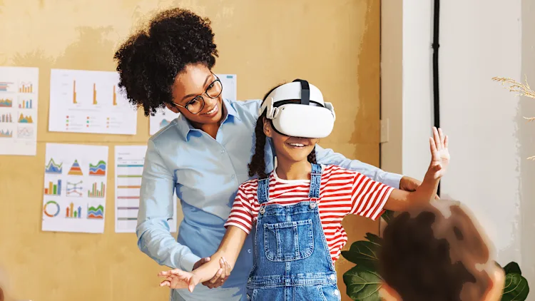 professora auxilia aluna no uso de óculos de realidade virtual