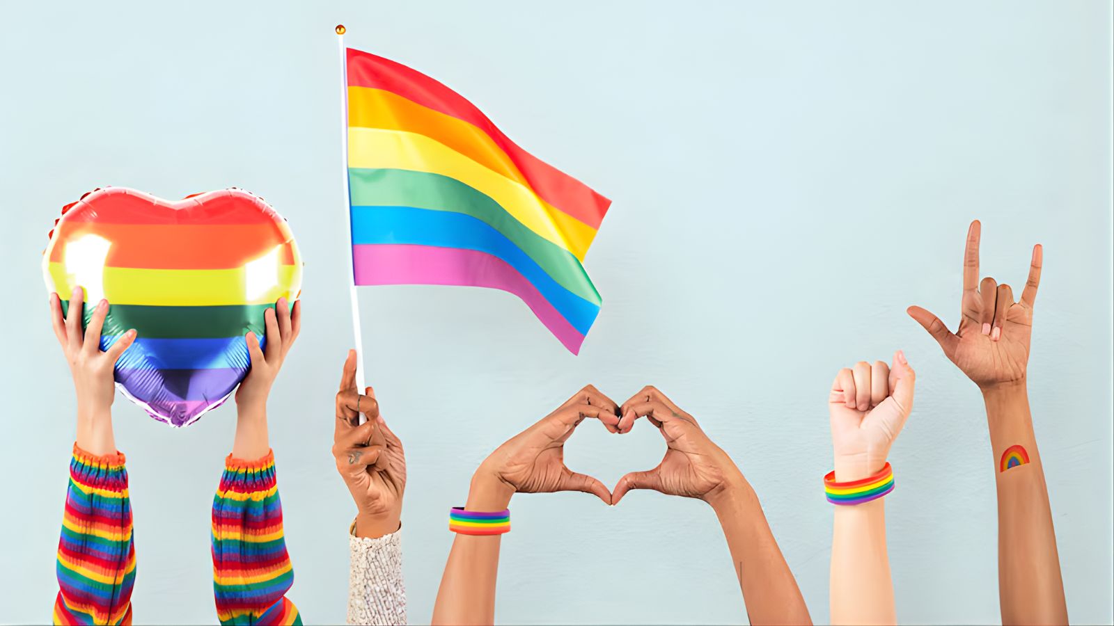 Mãos segurando bandeiras e balões com as cores do LGBTQIAPN+