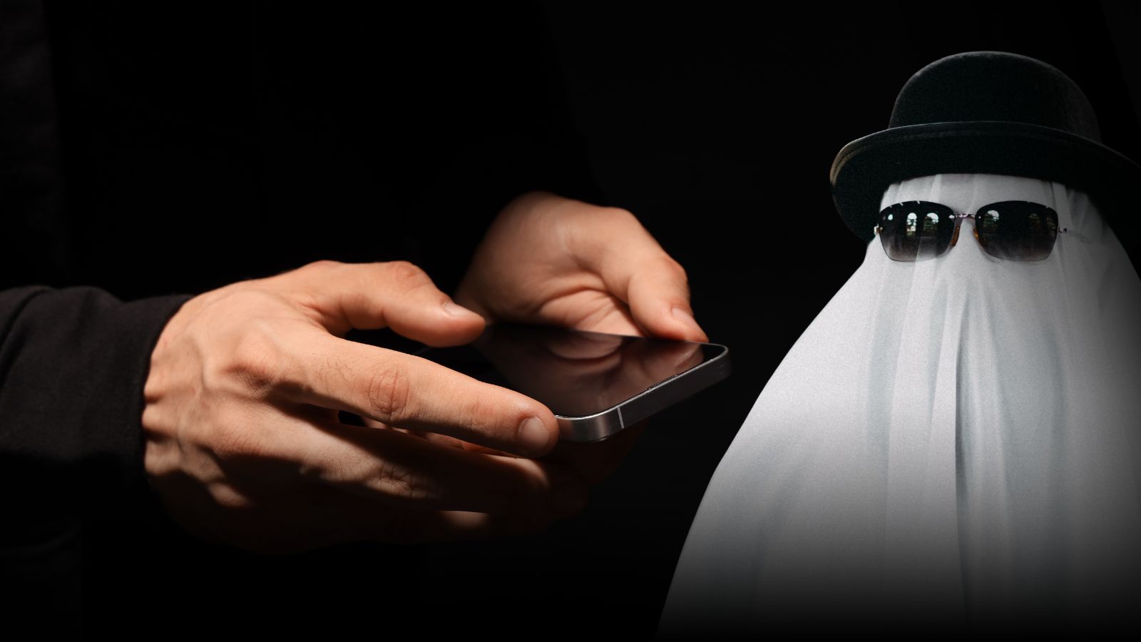 Mão segurando um celular e um fantasma de chapéu e óculos ao lado