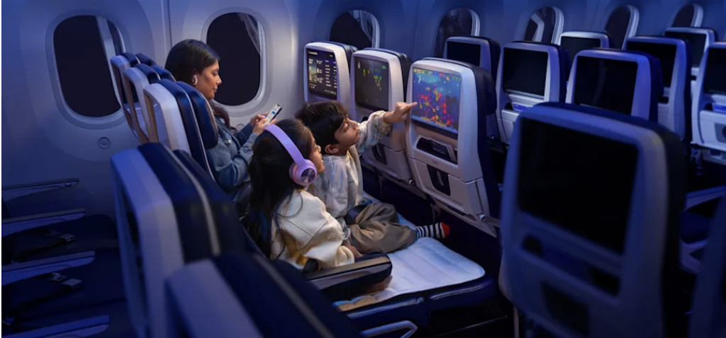 (mulher e duas crian&ccedil;as dentro de aeronave, uma delas usando fone e a outra brincando na tela)