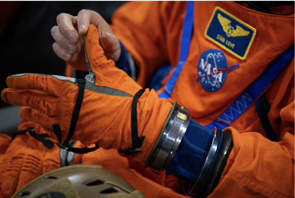 Detalhe de um tripulante da Artemis II, usando um macac&atilde;o laranja, mostrando os recursos tecnol&oacute;gicos para manter a vida dos astronautas mesmo em caso de acidente