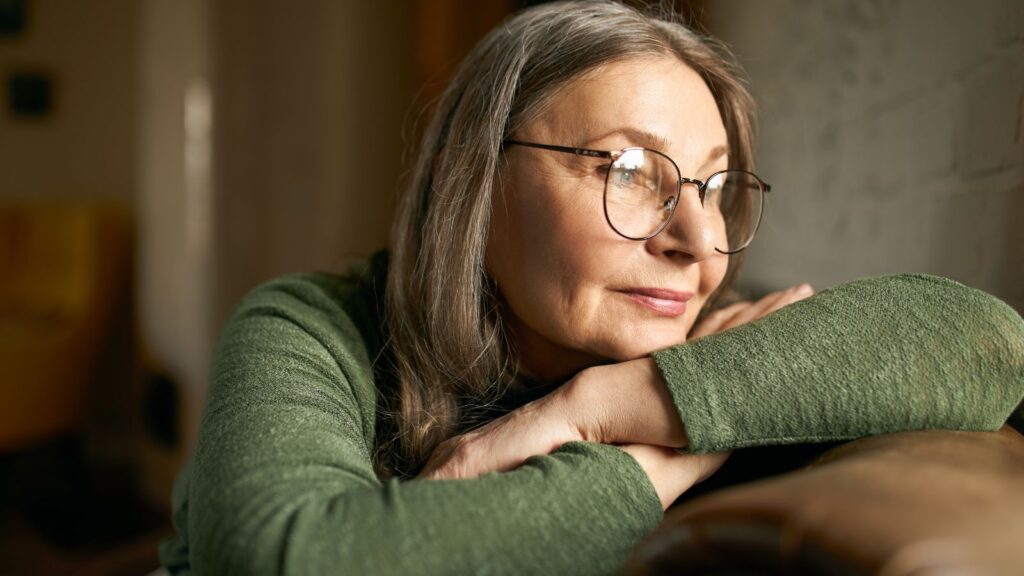 idosa com a cabeça sob os braços cruzados apoiados no sofá