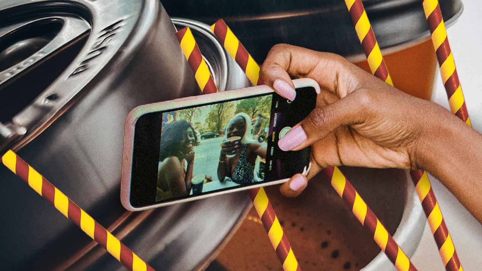 Uma mão segura um smartphone exibindo uma selfie em vídeo de duas pessoas sorrindo, cercada por canudos listrados e copos ao fundo. A imagem sugere cultura digital, registro espontâneo de momentos sociais, redes sociais e consumo ligado à experiência compartilhada.