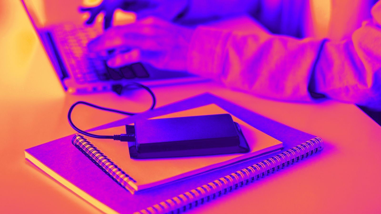 Mulher no computador enquanto se celular carrega em um carregador portatil