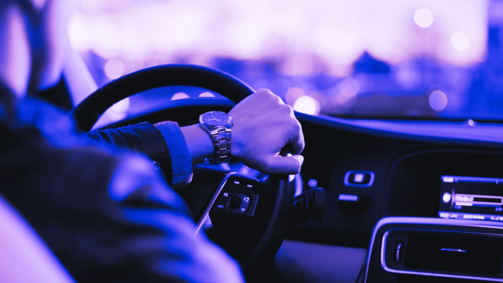 Homem dirigindo um carro, com a mão no volante