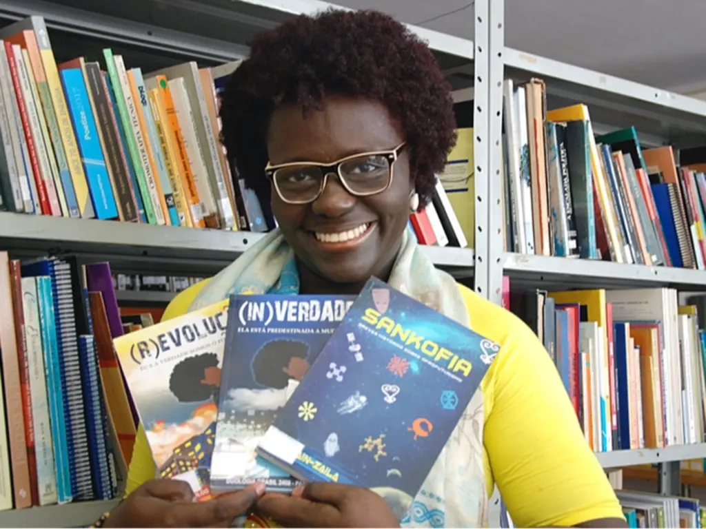 Lu Ain-Zaila sorri enquanto segura exemplares de seus livros diante de uma estante