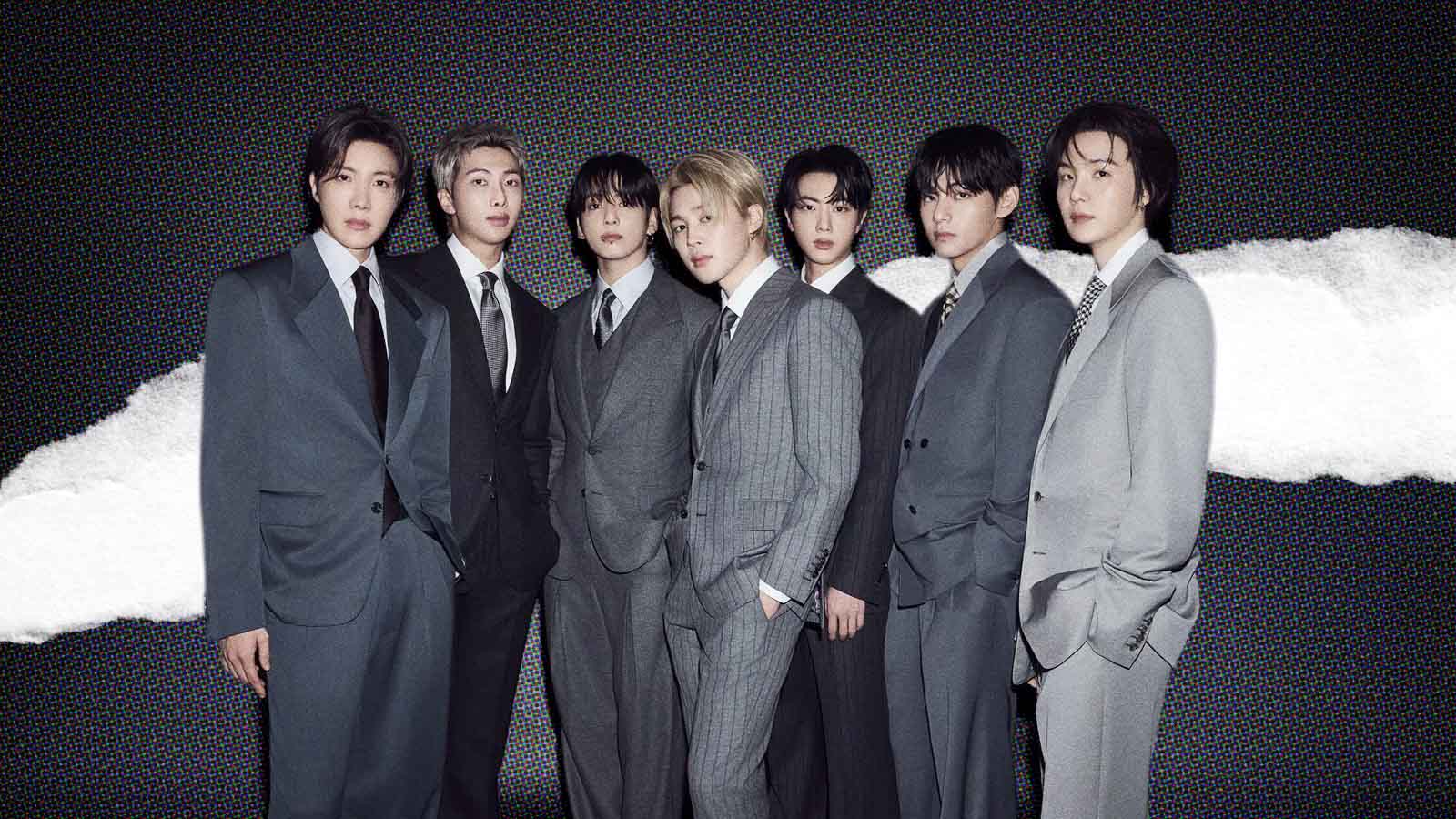 Integrantes do BTS posam com ternos cinza diante de um fundo preto.