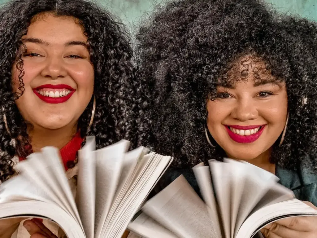 As irmãs Pérola e Isa Souza sorriem enquanto seguram livros abertos