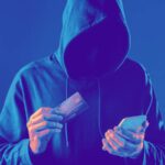 Homem de capuz segurando celular e cartão em fundo preto