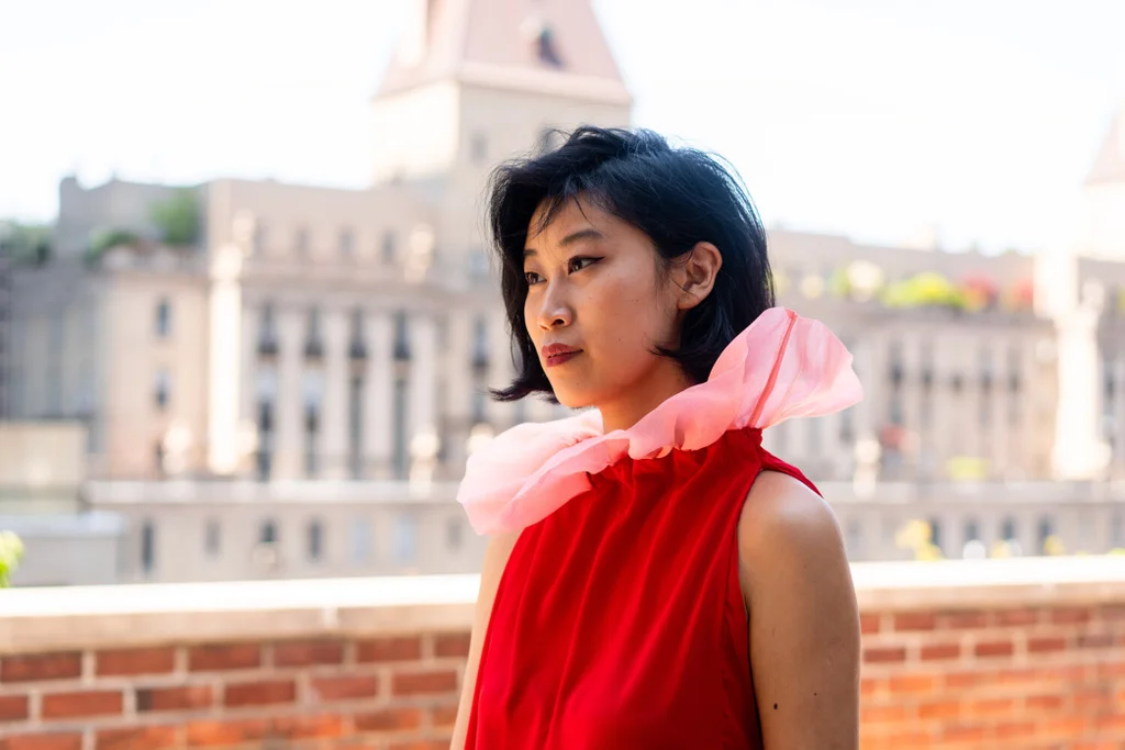 Shelly Xu, fundadora da SXD, veste uma pe&ccedil;a vermelha com gola rosa volumosa.