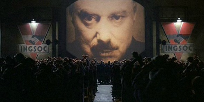 Multid&atilde;o reunida diante de uma tela gigante que exibe o rosto do Big Brother no filme 1984.