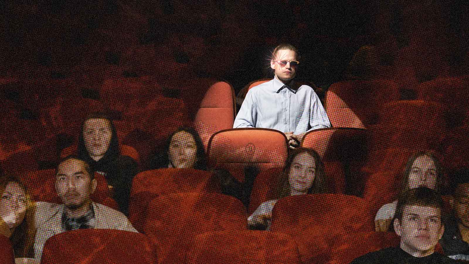 Pessoa com óculos inteligentes e um ponto de luz na lente sentada em uma sala de cinema.