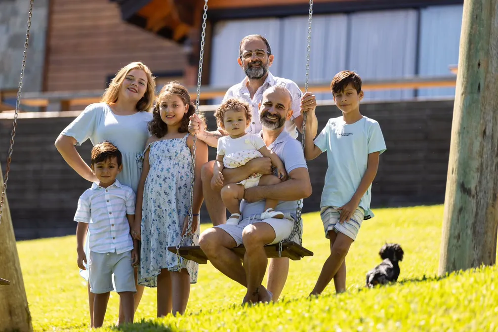Geninho Goes e Eduardo Domingos posam ao ar livre com os cinco filhos.