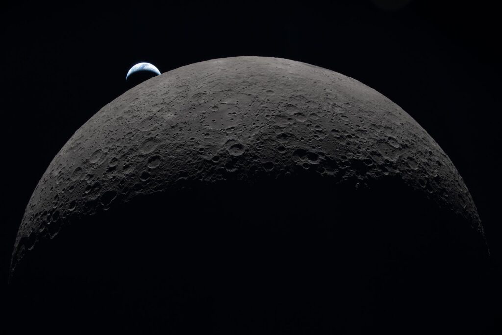 Superf&iacute;cie craterada da Lua com a Terra aparecendo ao fundo no espa&ccedil;o