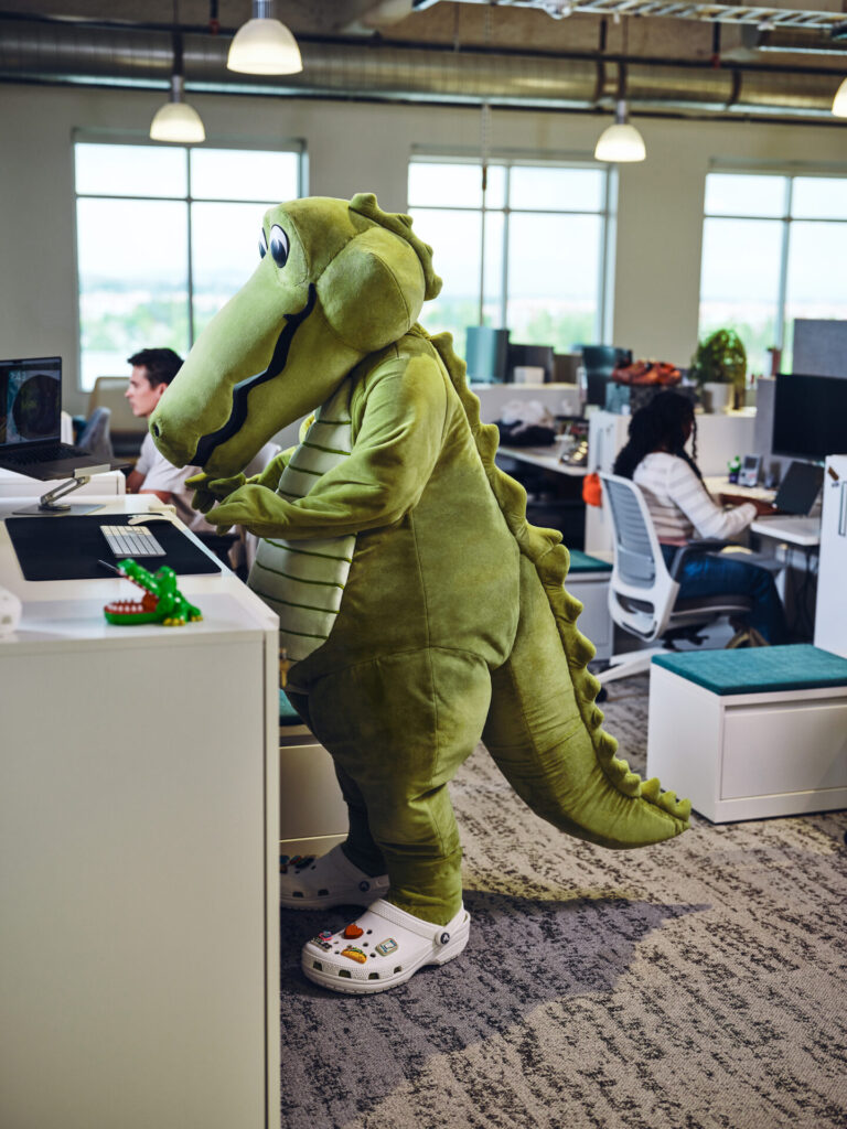 Niles, mascote da Crocs, usa tamancos brancos enquanto trabalha diante de um computador no escrit&oacute;rio da empresa.