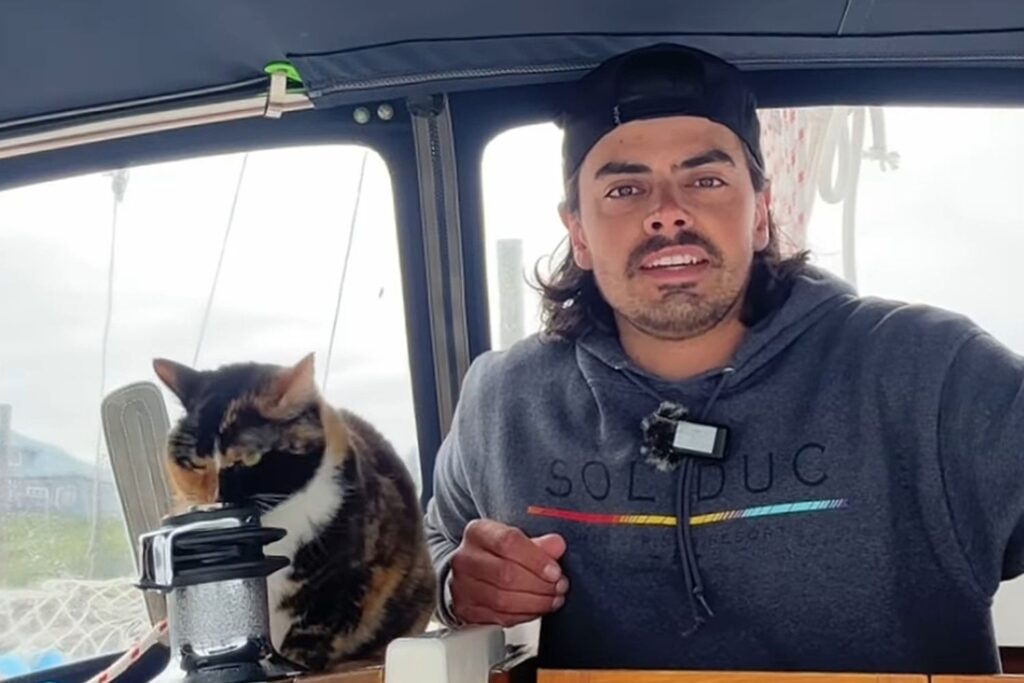 Oliver Widger aparece ao lado do gato Phoenix dentro de seu veleiro.