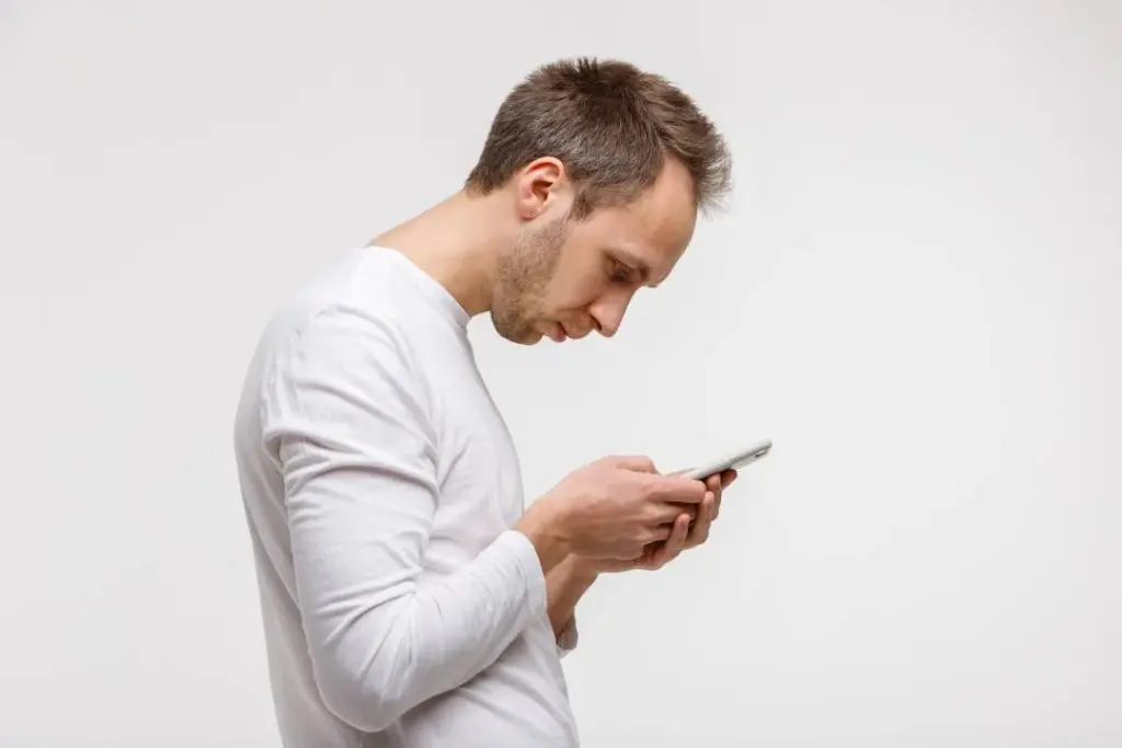 Homem olha para o celular com a cabe&ccedil;a e o pesco&ccedil;o inclinados para frente.