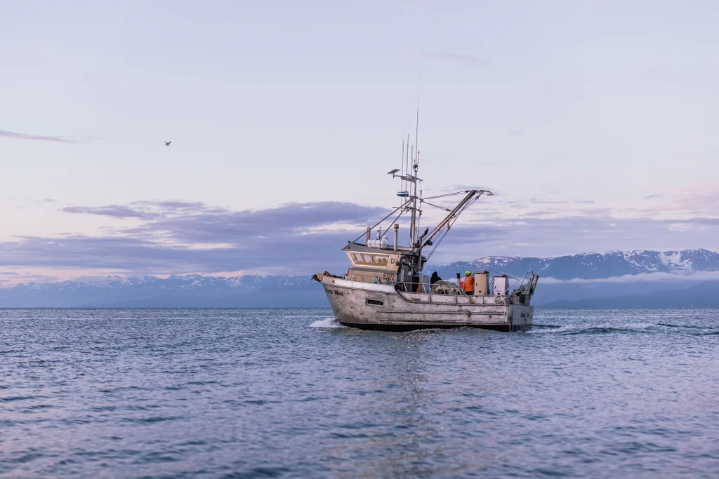 Barco de pesca navega em &aacute;guas do Alasca ao entardecer