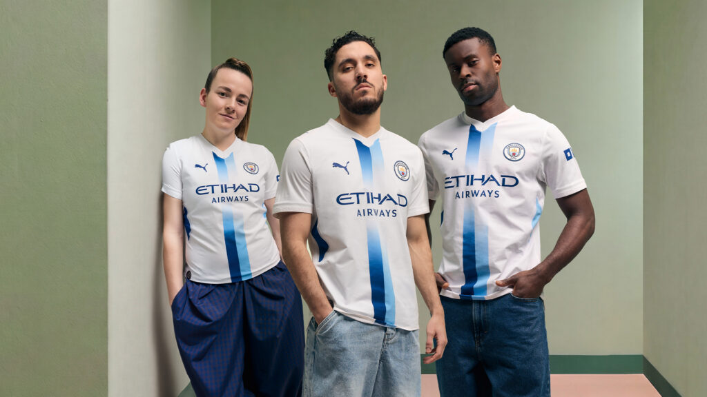 Tr&ecirc;s atletas do Manchester City posam com o uniforme branco criado por torcedores com intelig&ecirc;ncia artificial.