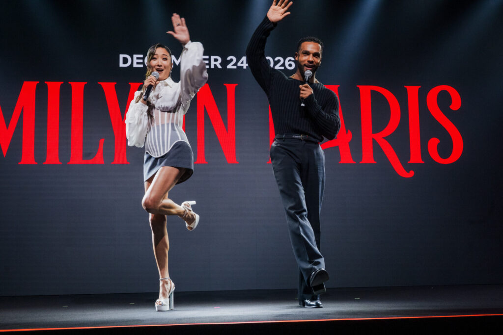 Ashley Park e Lucien Laviscount acenam no palco durante evento da Netflix em São Paulo.