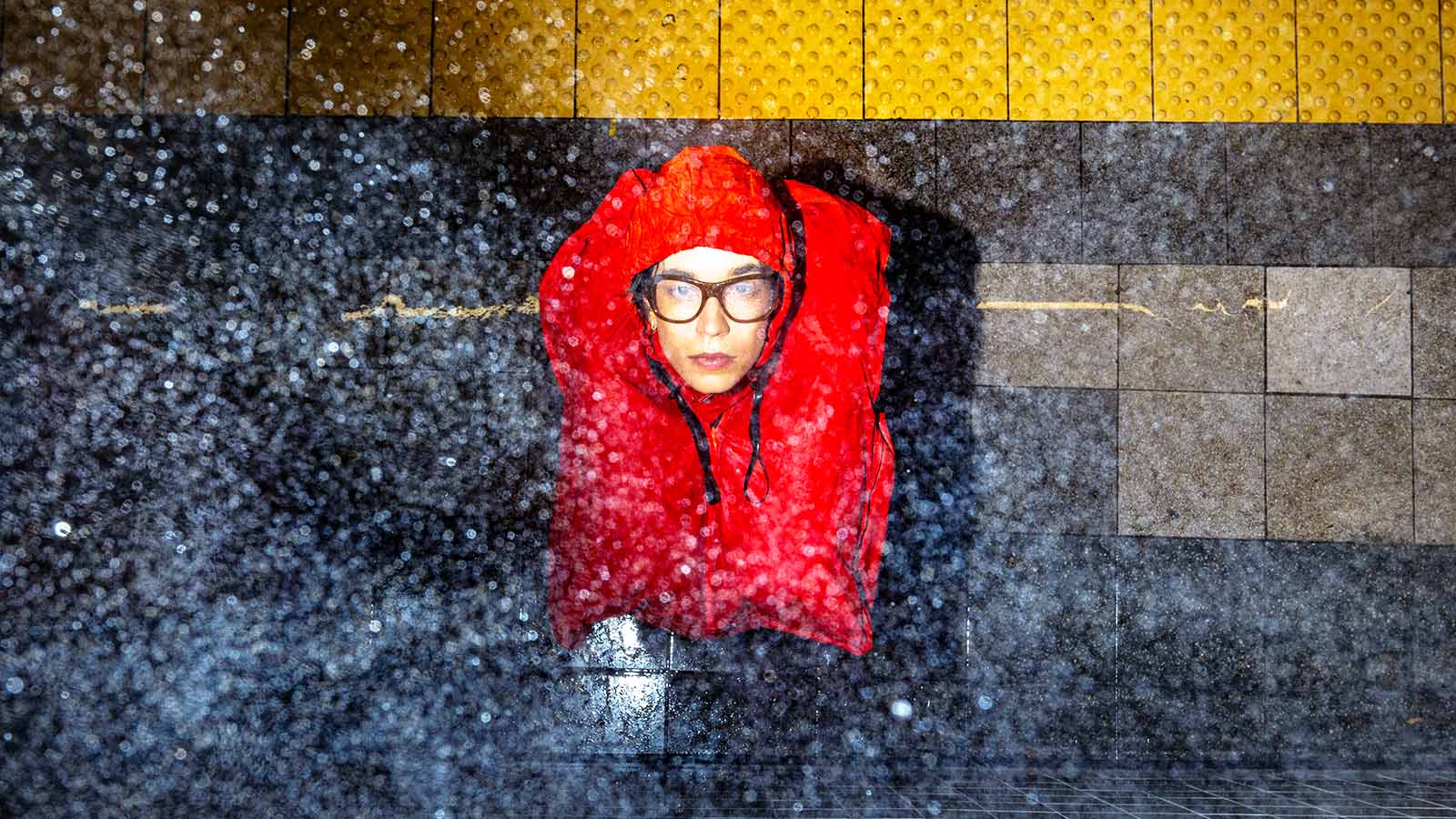 Pessoa usa colete salva-vidas vermelho sob chuva intensa em uma estação de metrô.
