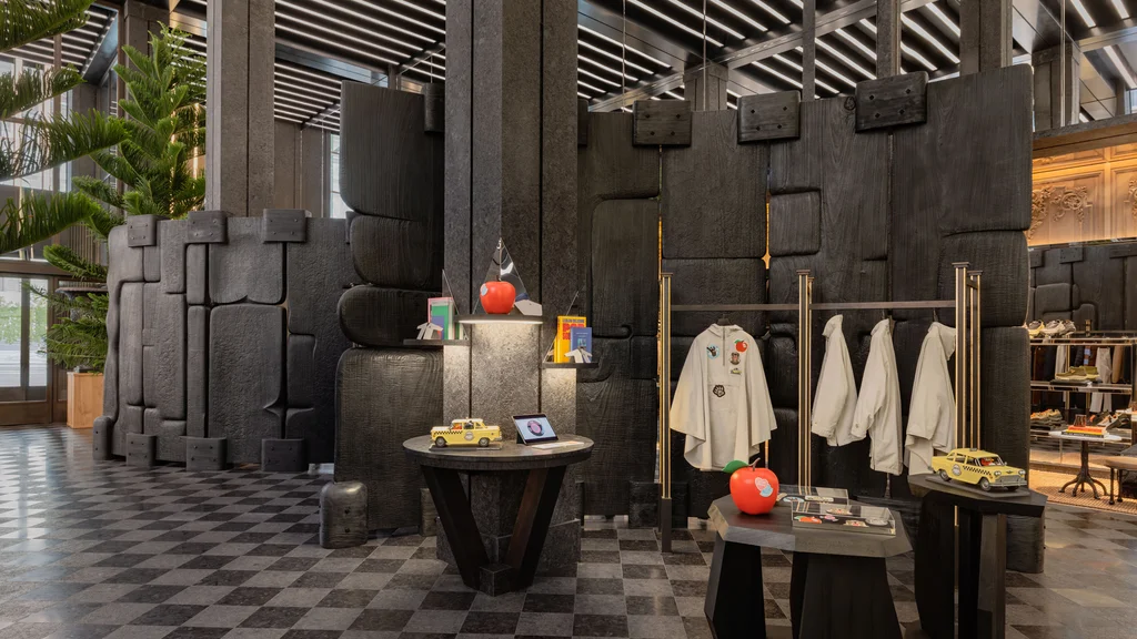 Instala&ccedil;&atilde;o da cole&ccedil;&atilde;o LoveFrom e Moncler em uma loja, com casacos claros pendurados entre estruturas pretas e objetos coloridos.
