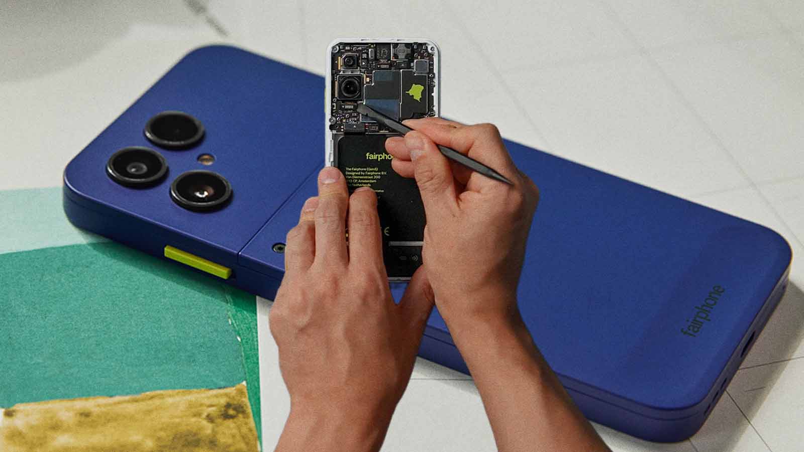 Mãos realizam reparo em um Fairphone aberto, diante da imagem ampliada de um celular azul.
