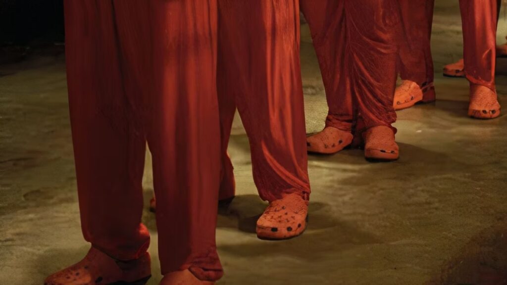 Personagens de Idiocracia usam calçados Crocs laranja combinando com seus uniformes.