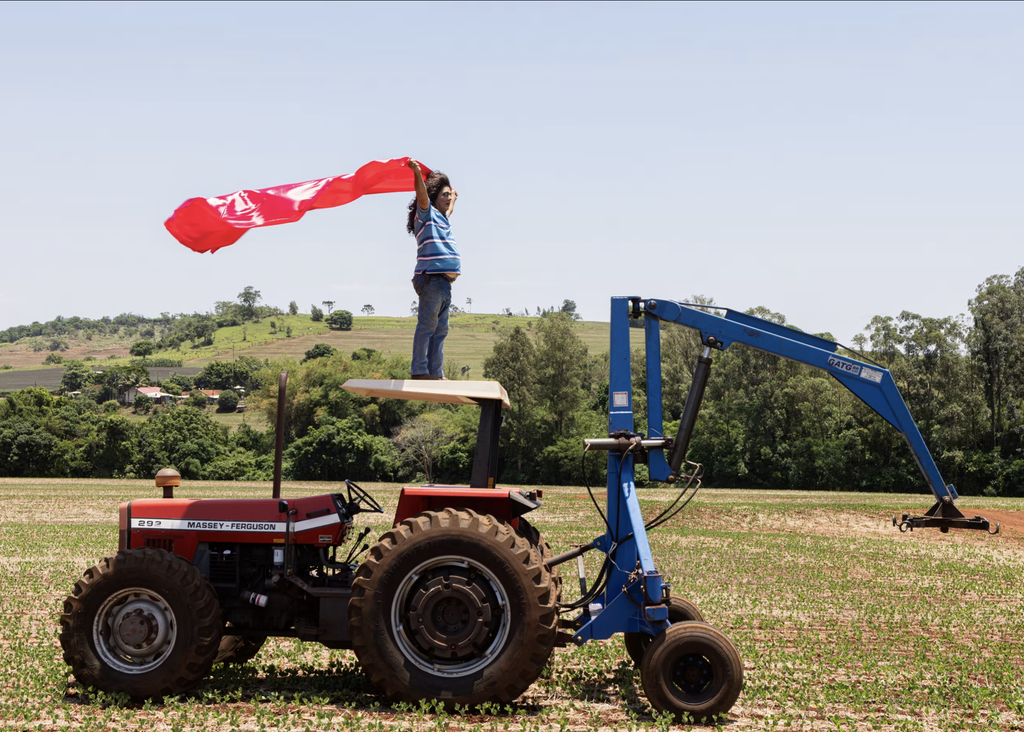 Pai de Danilo Zocatelli aparece maquiado e de peruca sobre um trator, segurando um longo tecido vermelho.