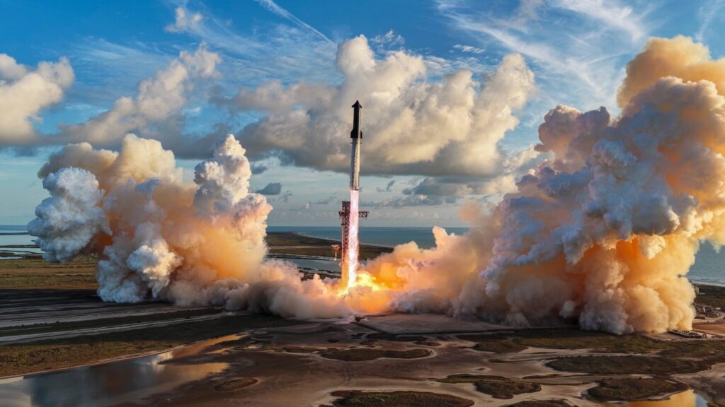 Starship decola ao lado da torre de lançamento, com chamas na base e grandes nuvens de fumaça sob o céu azul.