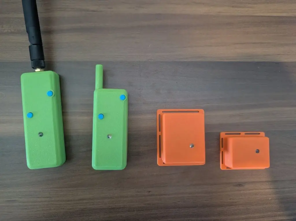 Quatro dispositivos eletrônicos verdes e laranja, de diferentes tamanhos, dispostos sobre uma mesa