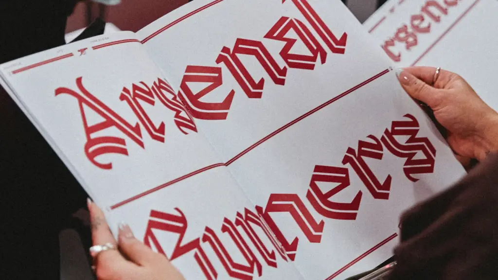 Pessoa segurando livro aberto com grandes letras vermelhas da tipografia Rocastle impressas sobre p&aacute;ginas brancas.