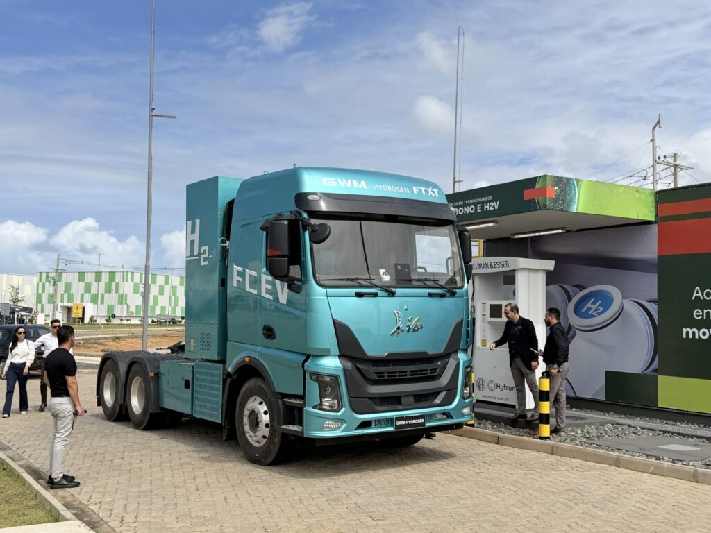 Caminh&atilde;o azul a hidrog&ecirc;nio da GWM estacionado ao lado de uma instala&ccedil;&atilde;o de hidrog&ecirc;nio, com pessoas pr&oacute;ximas ao ve&iacute;culo.