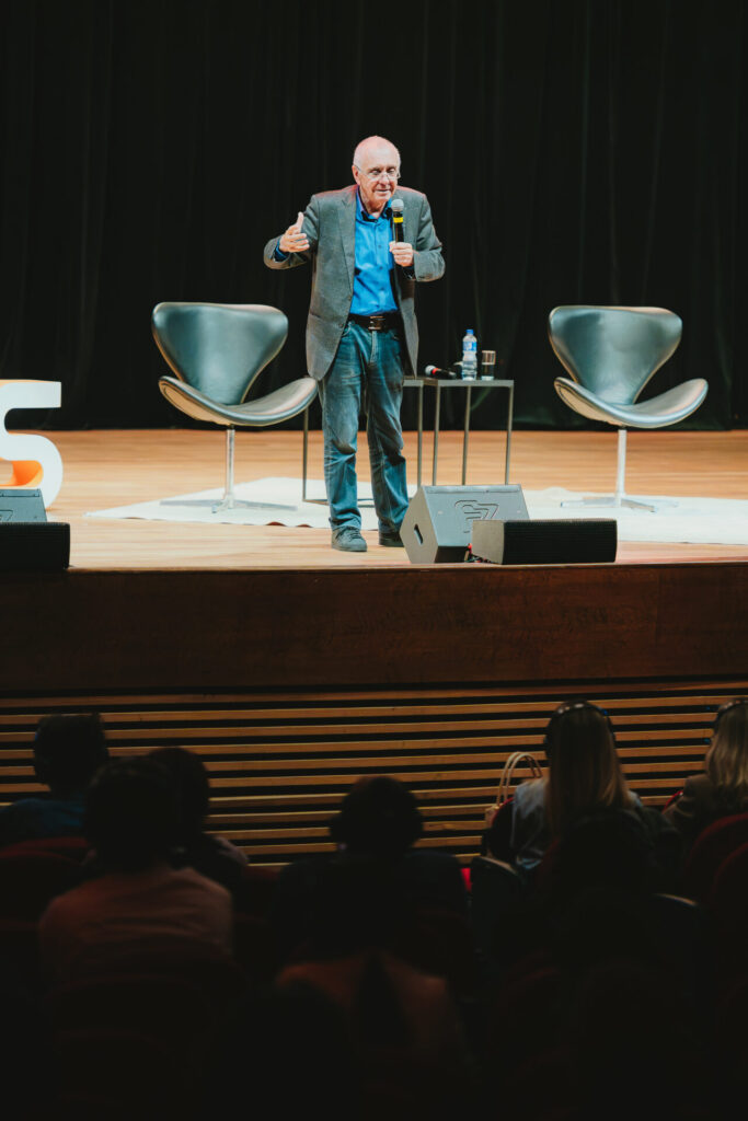Gilles Lipovetsky fala ao microfone no palco de um auditório, diante da plateia.
