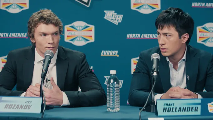 Cena de &ldquo;Heated Rivalry&rdquo; com Ilya Rozanov e Shane Hollander de terno, sentados diante de microfones em uma coletiva de imprensa.