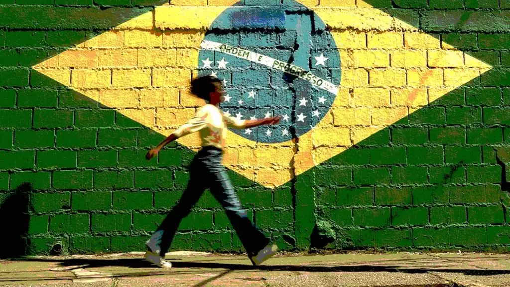 mulher caminha ao lado de uma parede decorada com a bandeira brasileira