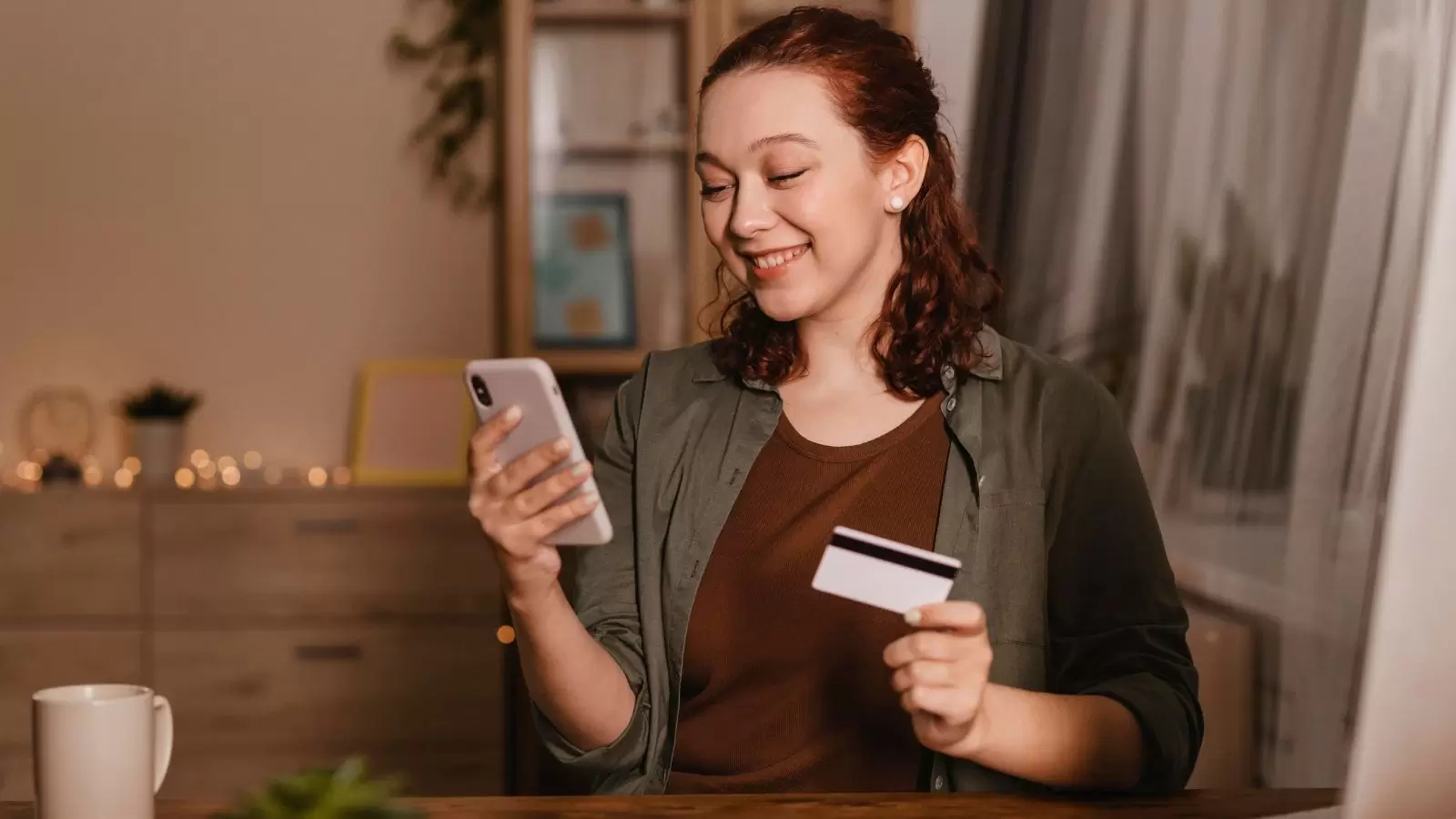 Mulher sorridente usando smartphone em casa com cartão de crédito