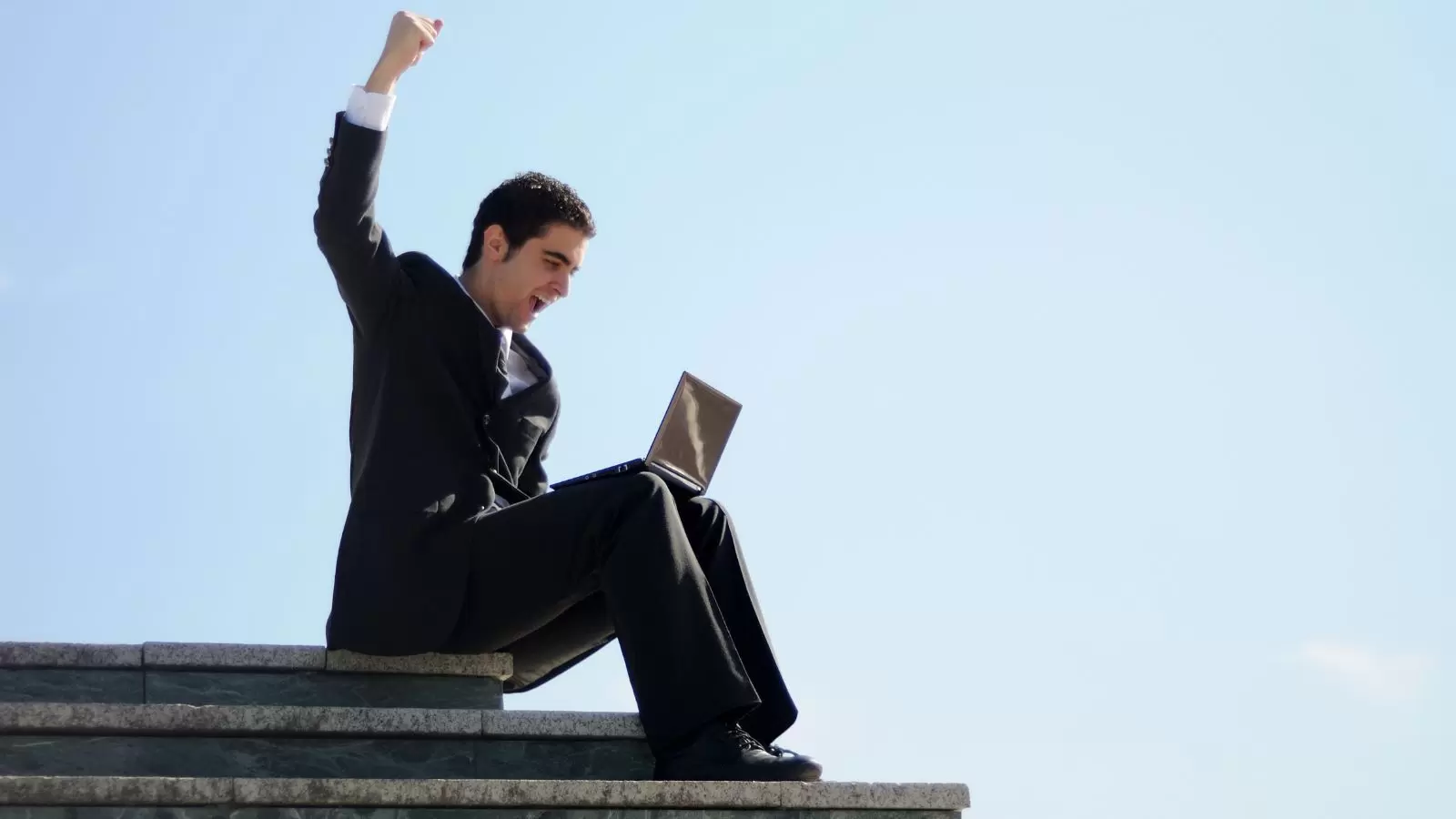 Homem sentado em escada com notebook comemorando