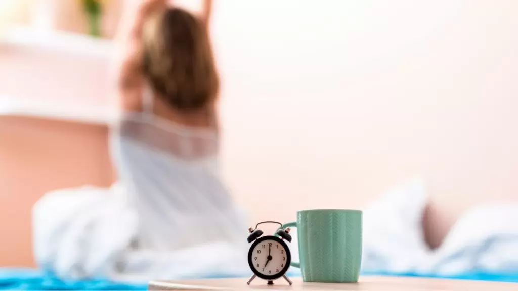 Mulher despertando com rel&oacute;gio e x&iacute;cara em foco na frente