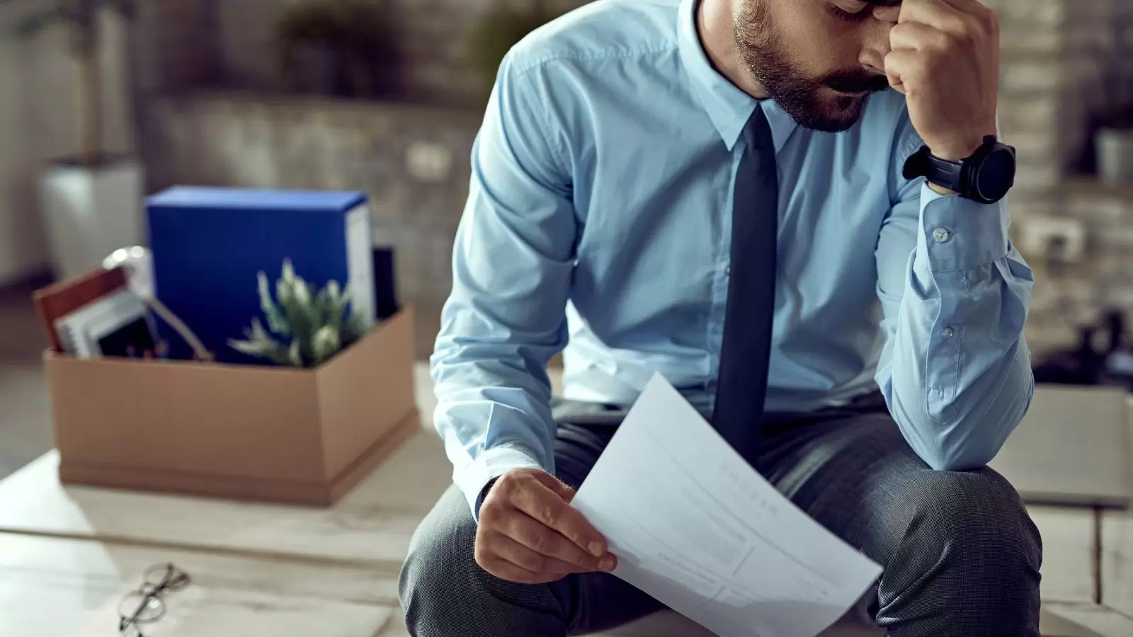 Homem sentado chorando após ser demitido