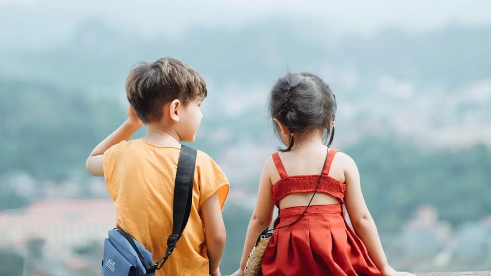 Um menino e uma menina de costa para paisagem