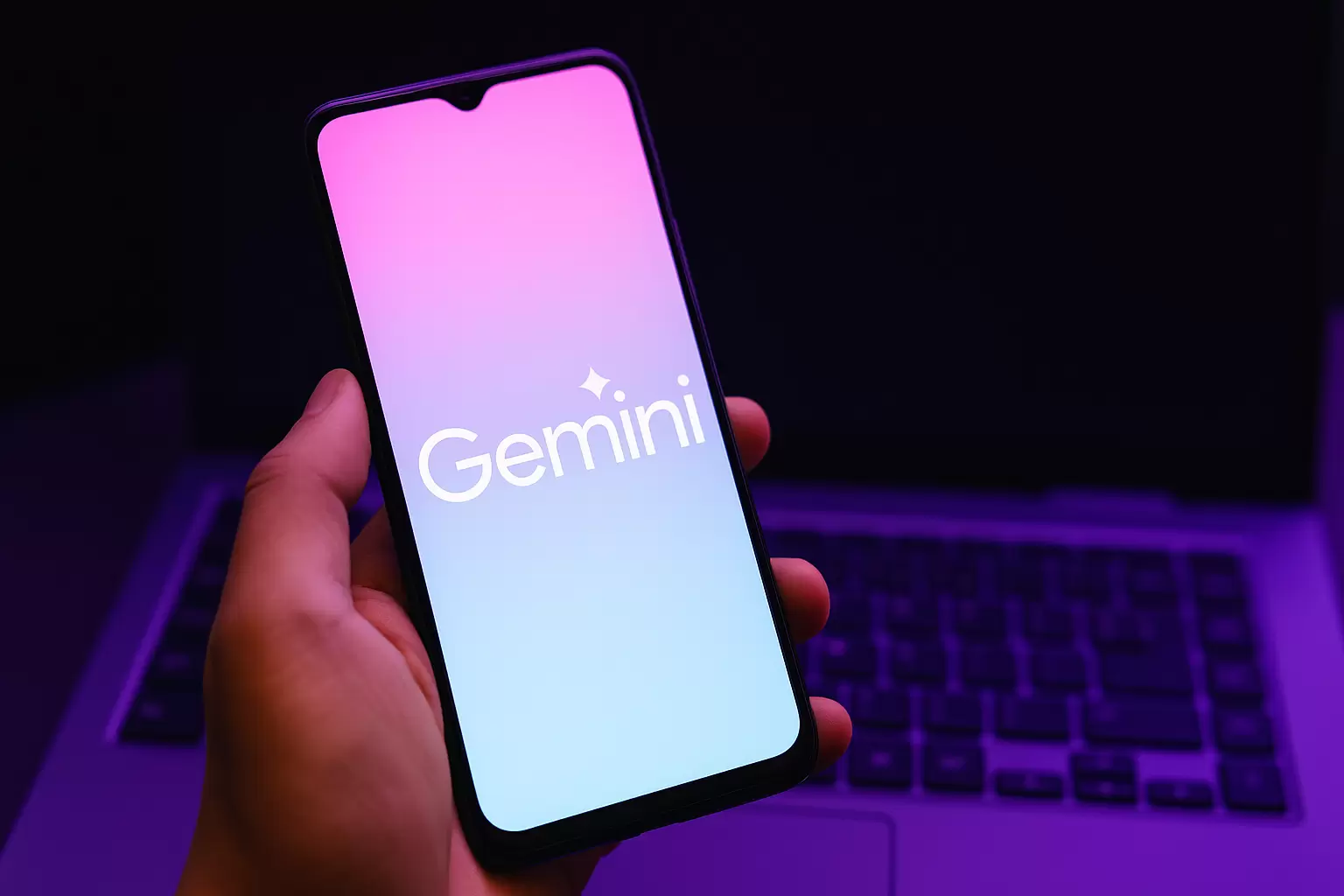 Pessoa segurando celular com o Gemini aberto, notebook ao fundo